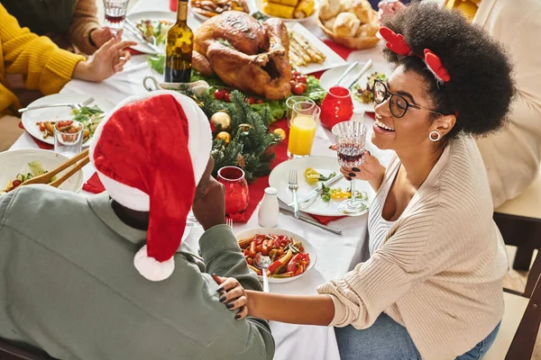 Alegre pareja afroamericana en la mesa de Navidad con su familia multiétnica, mano a hombro - foto de stock