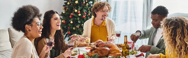 Grande famille multiethnique souriant et mangeant un déjeuner festif avec arbre de Noël sur fond, bannière — Photo de stock