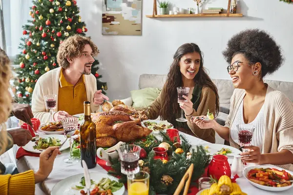 Веселі багаторасові члени сім'ї, сидячи за святковим столом і розмовляючи жваво, Різдво — стокове фото