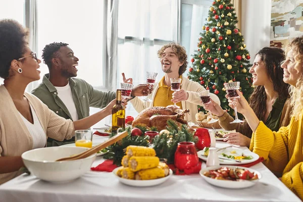 Gran familia multirracial riendo y haciendo gestos mientras disfruta del vino y el almuerzo festivo, Navidad - foto de stock