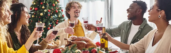 Famiglia multiculturale gesticolando e ridendo seduto al tavolo festivo che celebra il Natale, striscione — Foto stock