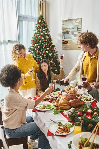 Heureux parents multiculturels assis à la table festive encourager et boire du vin, Noël — Photo de stock