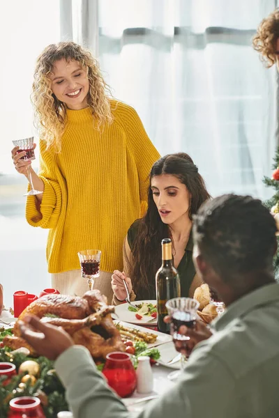 Feliz pareja lgbt rodeado de sus parientes multiétnicos disfrutando del vino y la comida, Navidad - foto de stock