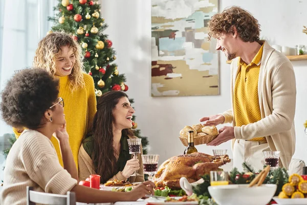 Jeune homme joyeux tenant assiette de pain entouré par sa famille multiethnique, toile de fond de sapin de Noël — Photo de stock
