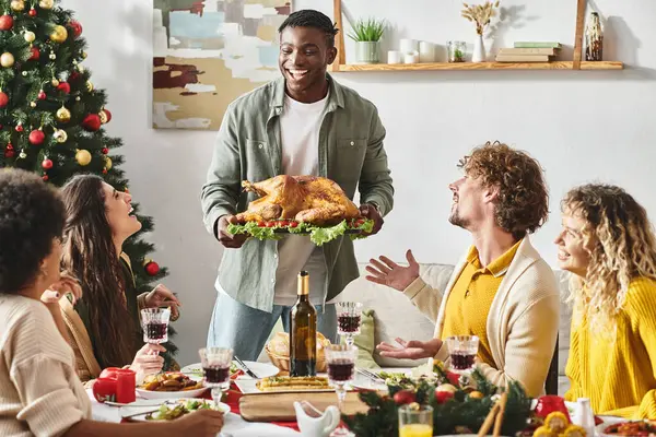 Feliz afro-americano sorrindo para seus parentes e segurando prato com peru, dia de Natal — Fotografia de Stock