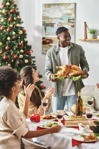 Big multicultural family gesturing and laughing and one holding plate with turkey, Christmas — Stock Photo