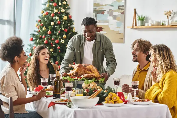 Allegri parenti multietnici che si preparano a mangiare delizioso tacchino seduto al banchetto di Natale — Foto stock