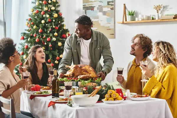 Vielvölkige Familie lächelnd einander am festlichen Tisch sitzend mit Wein und Truthahn, Weihnachten — Stockfoto