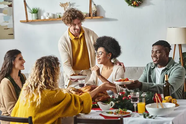 Família multicultural feliz sentada à mesa festiva compartilhando comida e bebendo vinho, Natal — Fotografia de Stock