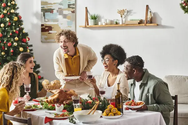 Familia multirracial alegre que se divierte mucho en el almuerzo festivo beber vino y comer pavo, Navidad - foto de stock