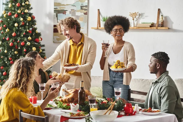 Glückliche multiethnische Verwandte, die Spaß daran haben, Weihnachten zu feiern, lächeln und Teller mit Essen halten — Stockfoto