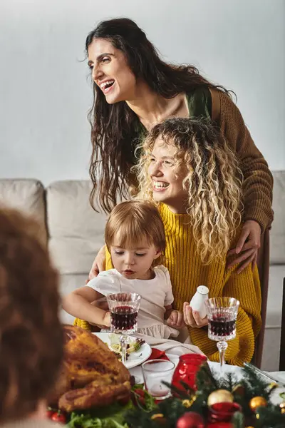Young lgbt couple with their daughter sitting at Christmas table surrounded by their relatives — Stock Photo