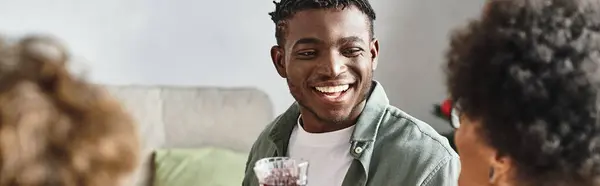 Homem americano africano alegre sentado na mesa de Natal sorrindo e levantando copo de vinho, bandeira — Fotografia de Stock