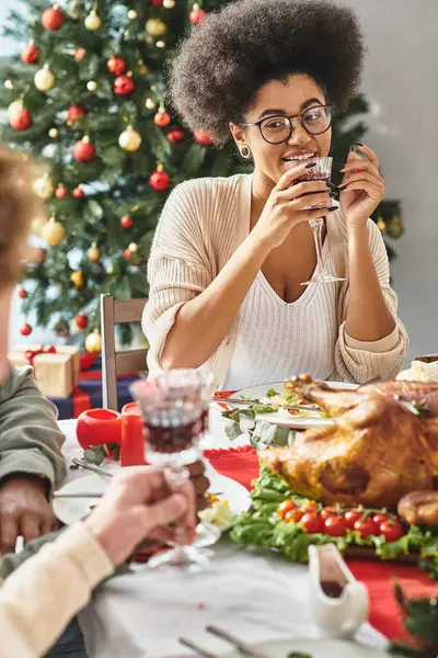 Mulher americana africana alegre falando com seus parentes bebendo vinho com fundo de árvore de Natal — Fotografia de Stock