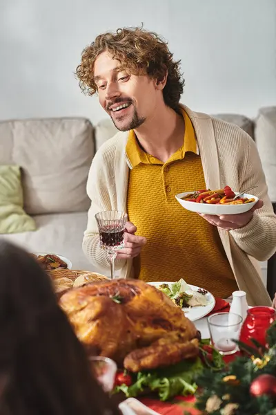 Jovem homem alegre sentado na mesa de férias com sua família e desfrutar de comida festiva, Natal — Fotografia de Stock