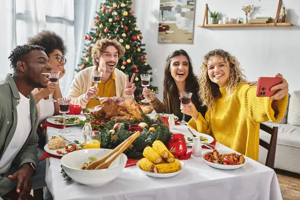 Big multiracial family taking joyful selfie sitting at festive table with Christmas tree on backdrop — Stock Photo