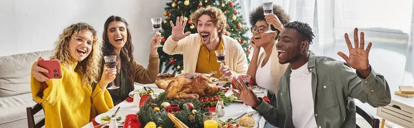 Joyful multiracial family taking selfies at holiday lunch with Christmas tree on backdrop, banner — Stock Photo