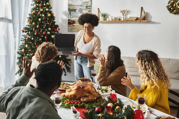 Multicultural family gathered at festive lunch waving smiling cheerfully at laptop camera, Christmas — Stock Photo