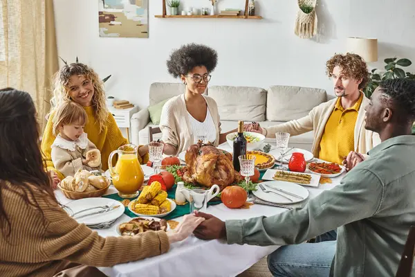 Joyful multicultural family members sitting and holding hands praying at festive table, Thanksgiving — Stock Photo