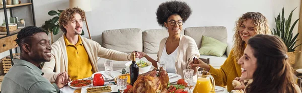 Famille multiethnique souriante assise et tenant la main à la table des fêtes, Action de grâces, bannière — Photo de stock