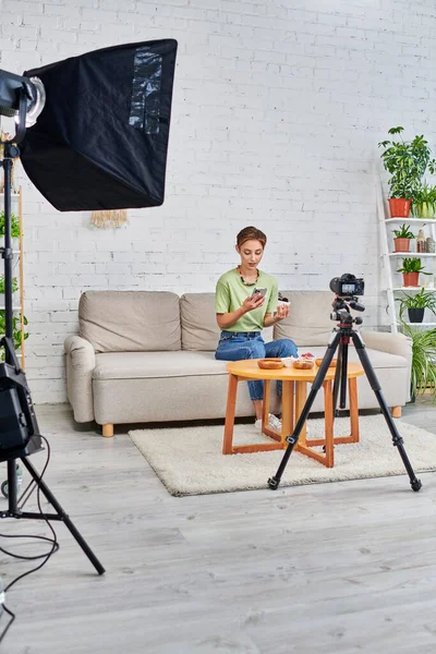 Blogueiro de vídeo com smartphone perto do conjunto de comida vegetariana e câmera digital com lâmpada softbox — Fotografia de Stock