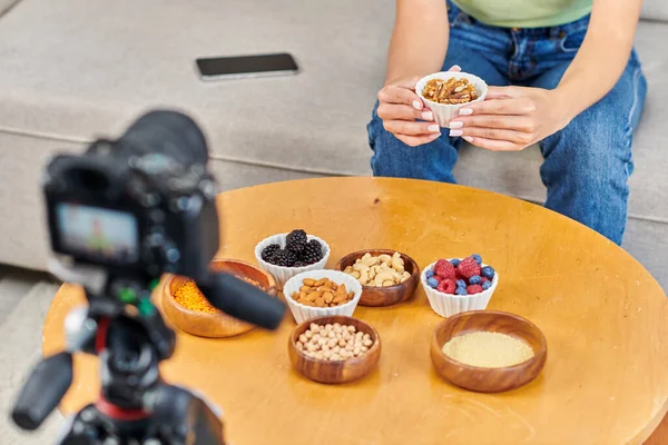 Vista recortada de video blogger con nueces cerca de varios ingredientes vegetarianos y cámara digital - foto de stock