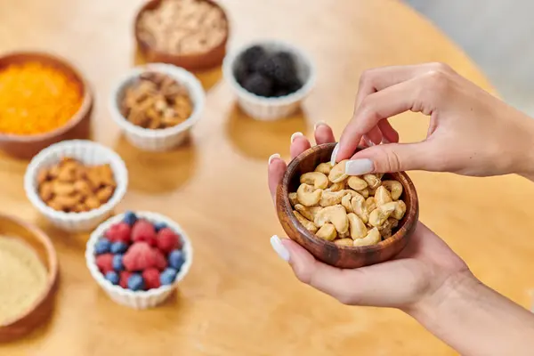 Cropped view of woman with bowl of cashews above different plant-based products on blurred table — Stock Photo