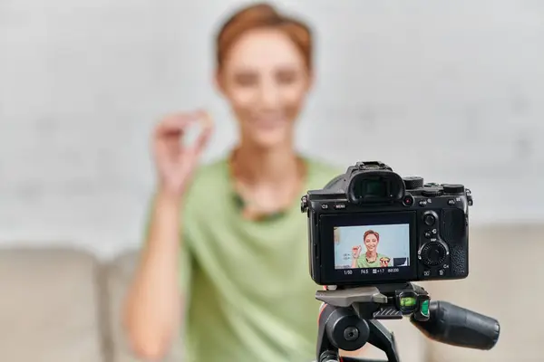 Focus on digital camera in front of happy vegetarian woman with plant-based food, content creation — Stock Photo