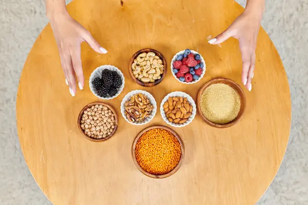 Vista superior de las manos femeninas sobre la mesa con una variedad de alimentos vegetarianos a base de plantas en la mesa en casa - foto de stock