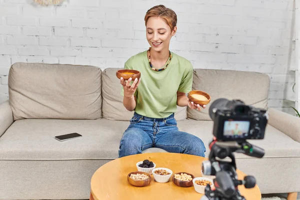 Щаслива жінка з мисками кус-кус та сочевиці біля цифрової камери та різноманітної рослинної їжі — стокове фото