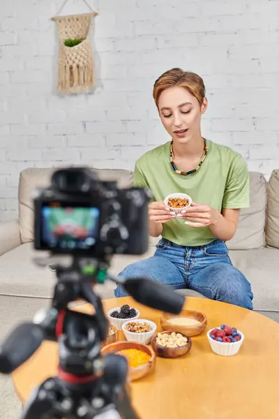 Female video blogger with bowl of almonds near plants-based food and blurred camera, vegetarianism — Stock Photo