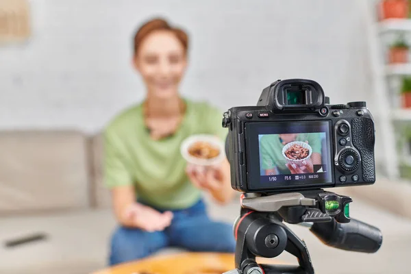 Enfoque en la cámara digital cerca de la mujer vegetariana con un tazón de nueces, las dietas a base de plantas video blog - foto de stock