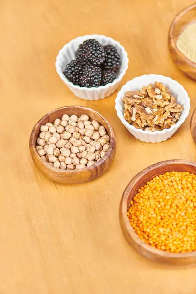Mûres près de noix et lentilles avec pois chiches dans des bols sur la table, régimes à base de plantes, vue de dessus — Photo de stock