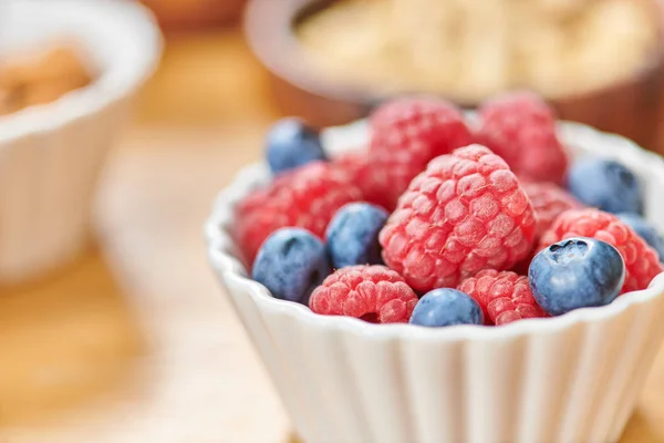 Close up view of ripe raspberries and blueberries in white bowl on blurred background, vegetarianism — Stock Photo