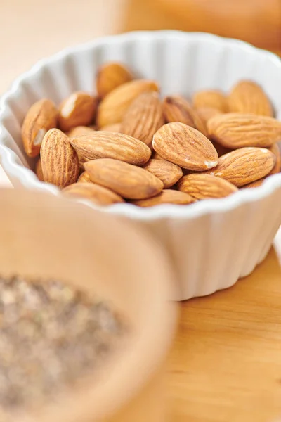 Close up view of delicious almonds in white ceramic bowl on blurred foreground, plant-based diets — Stock Photo