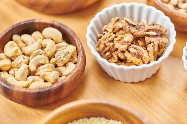 Vista de ángulo alto de cuencos con anacardos y nueces en la mesa, comida vegetariana saludable alta en calorías - foto de stock