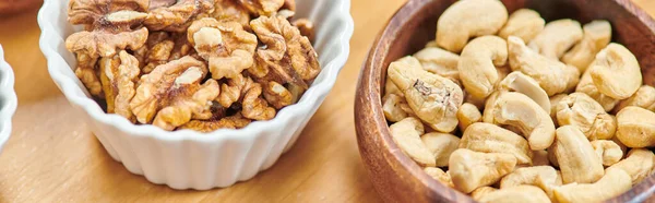 Вид на высококалорийные кешью и грецкие орехи в мисках на столе, концепция диет на основе растений, баннер — стоковое фото
