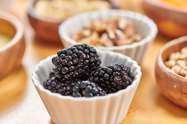 Close up of bowl with sweet ripe blackberries near variety of plant-based food on blurred background — Stock Photo