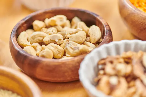 Gros plan de délicieuses noix de cajou à haute teneur en calories dans un bol en bois près des aliments à base de plantes, concept végétarien — Photo de stock
