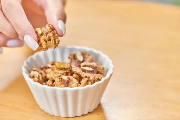 Cropped view of female hand taking walnut from white ceramic bowl, high-calorie plant-based food — Stock Photo