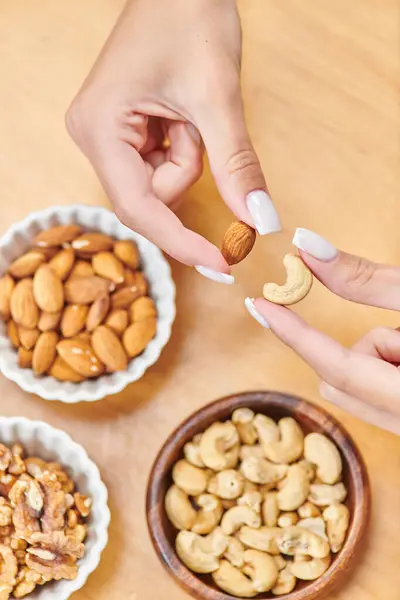 Cropped view of woman holding cashew and walnut above bowls with nuts, high calorie plant-based food — Stock Photo