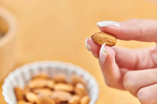 Close up view of female hand with almond above bowl with vegetarian food on blurred background — Stock Photo