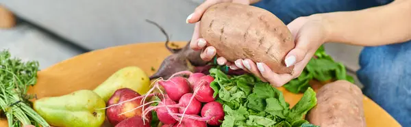 Частичный вид вегетарианки, держащей сладкий картофель над редиской и свежими фруктами, баннер — стоковое фото