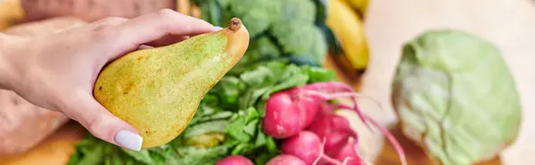 Mano de mujer vegetariana con delicioso muelle por encima de verduras y frutas borrosas, bandera horizontal - foto de stock
