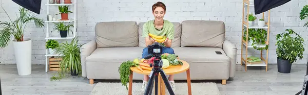 Blogueiro de vídeo vegetariano perto de legumes e frutas na sala de estar verde com câmera digital, banner — Fotografia de Stock