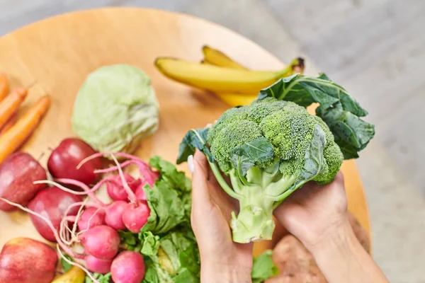 Vue du dessus des mains féminines avec brocoli frais sur les légumes et les fruits sur la table, régime à base de plantes — Photo de stock