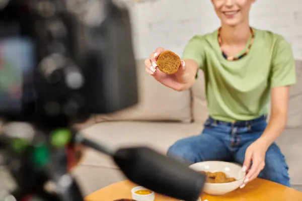 Обрезанный вид счастливой женщины показывает домашние вегетарианские котлеты возле размытой цифровой камеры, vlogger — стоковое фото