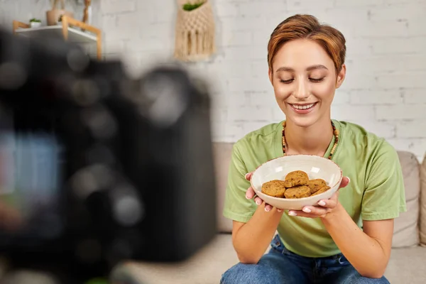 Mulher vegetariana satisfeito com tigela de costeletas vegetais perto de câmera digital borrada, blog de vídeo — Fotografia de Stock