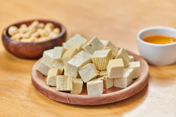 Vista de cerca del queso tofu picado cerca de nueces de anacardo y aceite de oliva en la mesa, cocina a base de plantas - foto de stock