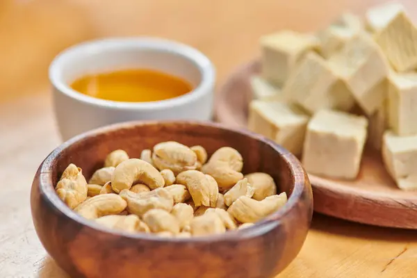 Concepto de dietas a base de plantas, primer plano de nueces de anacardo y queso tofu cortado en cubitos cerca del aceite de oliva natural - foto de stock